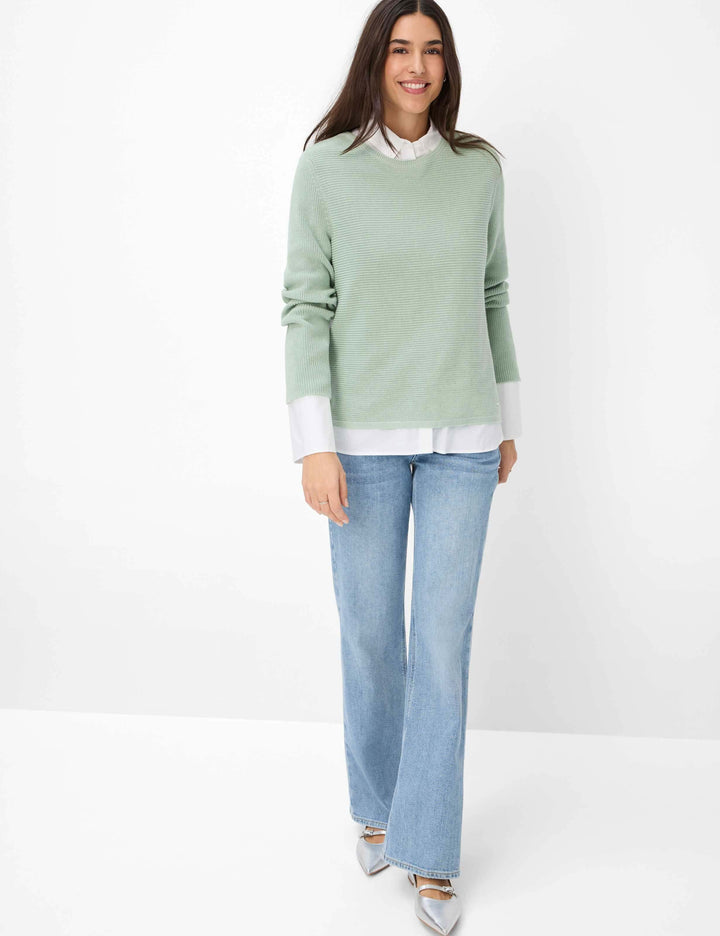 Femme portant un pull vert menthe et un jeans palazzo en denim, look contemporain et décontracté.