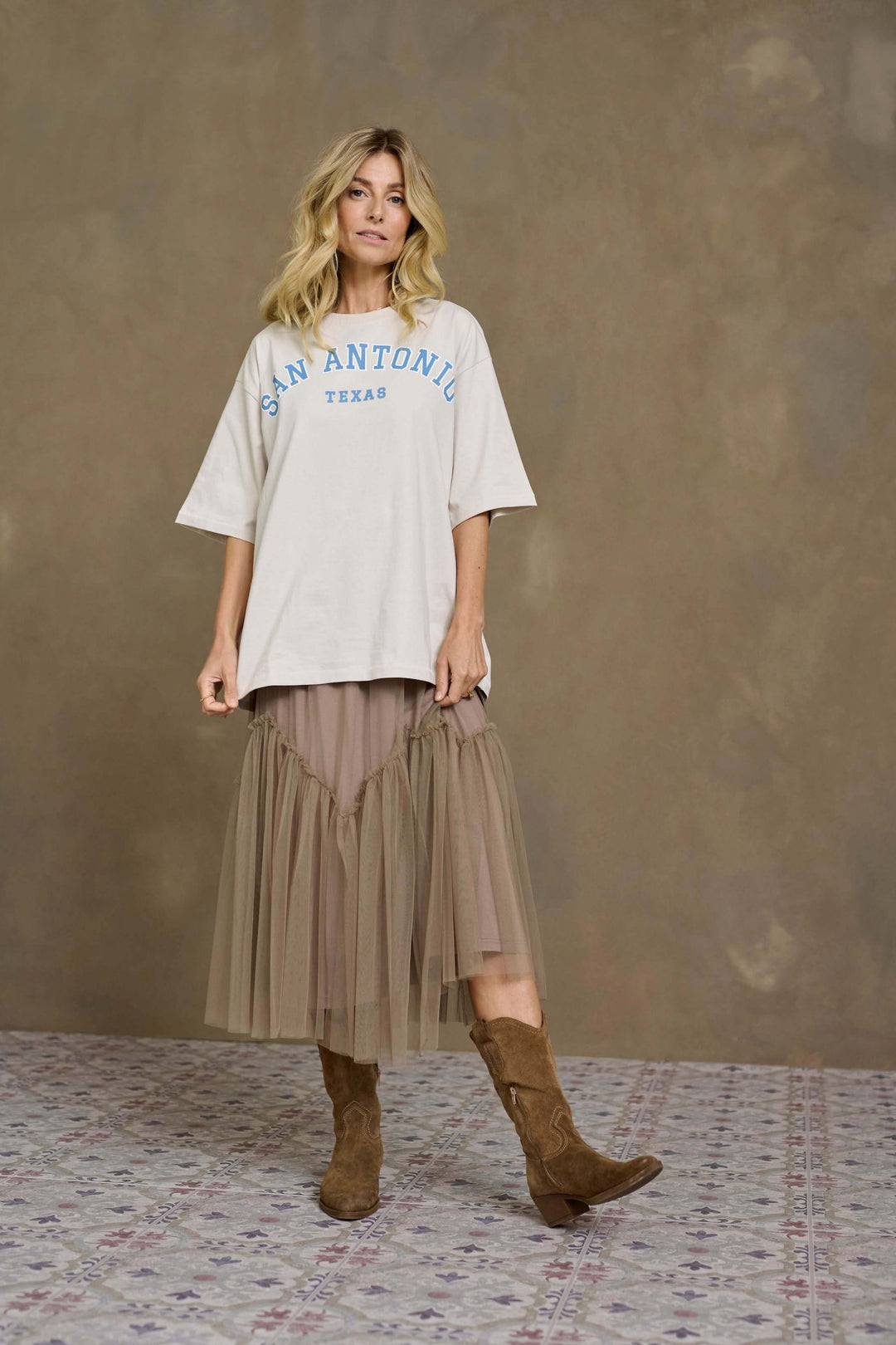 Femme en t-shirt oversized avec imprimé San Antonio, jupe midi en tulle et bottes en suédine.