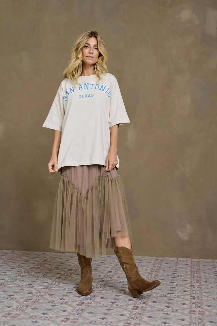 Femme en t-shirt oversized avec imprimé San Antonio, jupe midi en tulle et bottes en suédine.