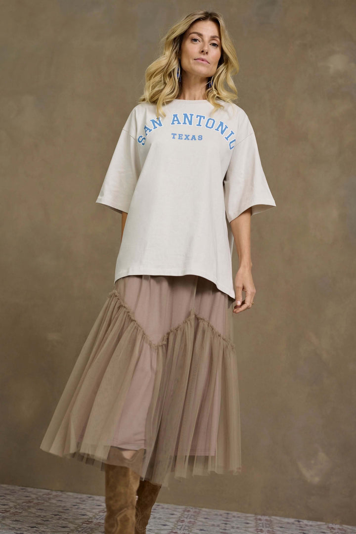 Femme en t-shirt beige avec inscription San Antonio, portant une jupe midi en tulle vaporeux beige.
