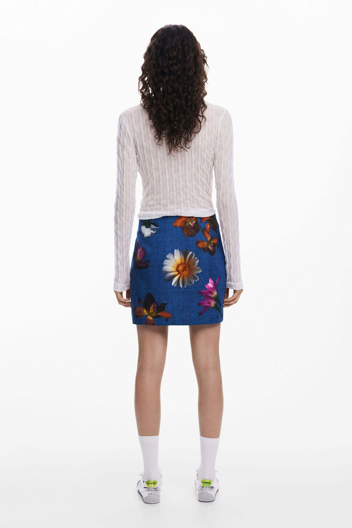 Femme de dos portant une jupe courte à fleurs avec un haut à manches longues, style décontracté et moderne.