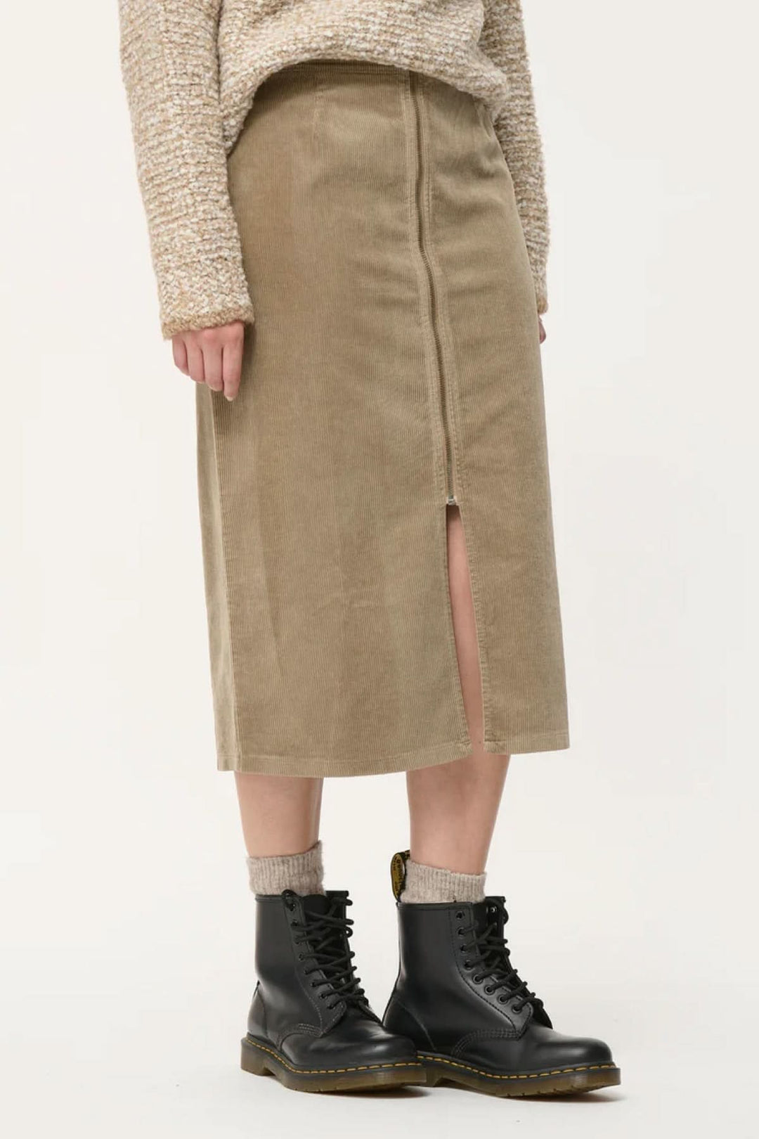 Jupe crayon en velours côtelé, taille haute, avec fente, portée avec des bottes noires.