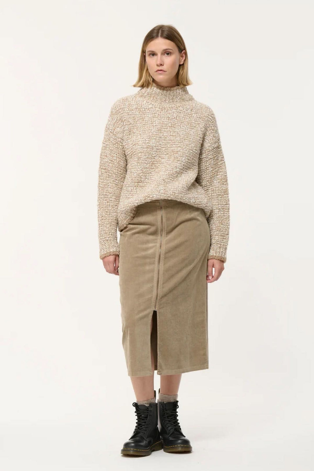 Femme portant une jupe crayon taille haute en velours côtelé avec un pull beige et des bottes noires.