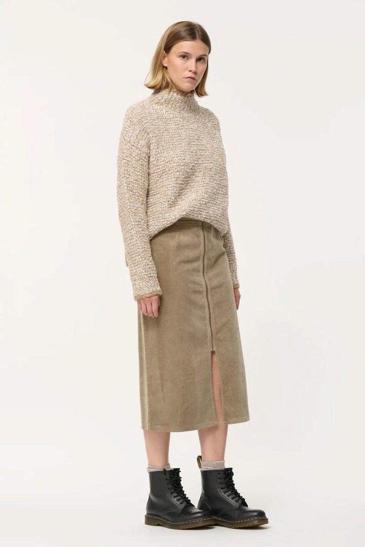 Femme portant une jupe crayon taille haute en velours côtelé avec un pull beige, style chic et décontracté.