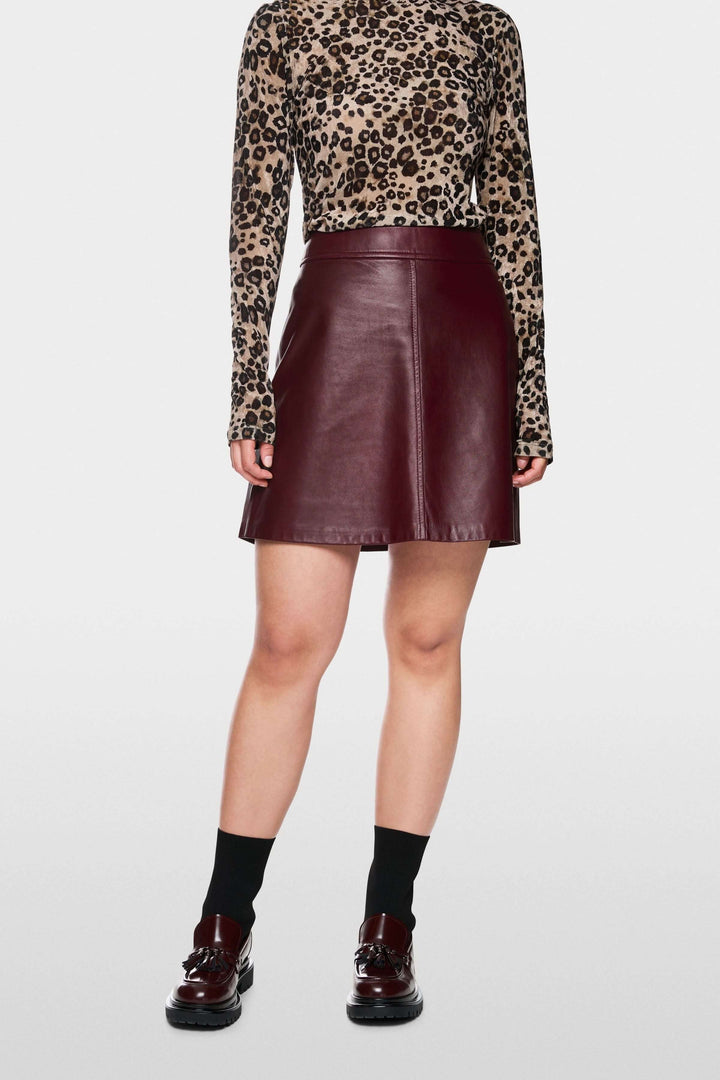 Jupe en cuir bordeaux coupe trapèze, portée avec un haut à motifs léopard, style moderne et élégant.