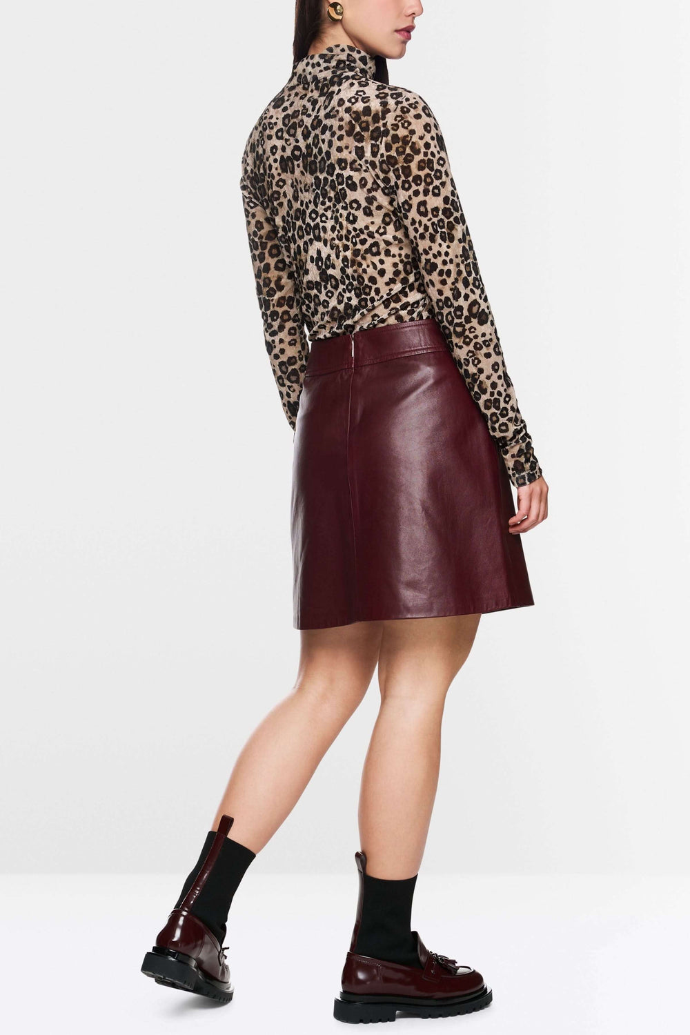 Jupe en cuir rouge mi-haute, coupe trapèze, portée avec un haut à motif léopard et des bottines chic.