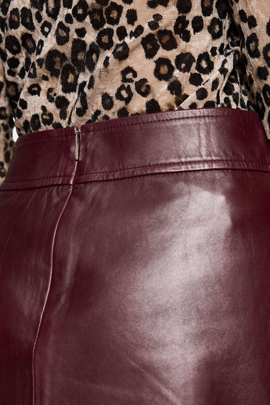 Détail d'une jupe en cuir bordeaux, mettant en avant la taille et la texture, portée avec un haut à motifs léopard.