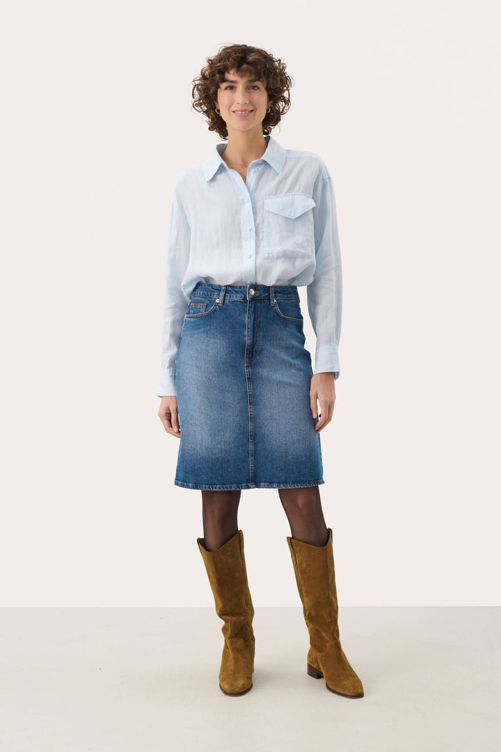 Femme portant une jupe en denim Leja avec une chemise claire et des bottes, affichant un look décontracté et stylé.