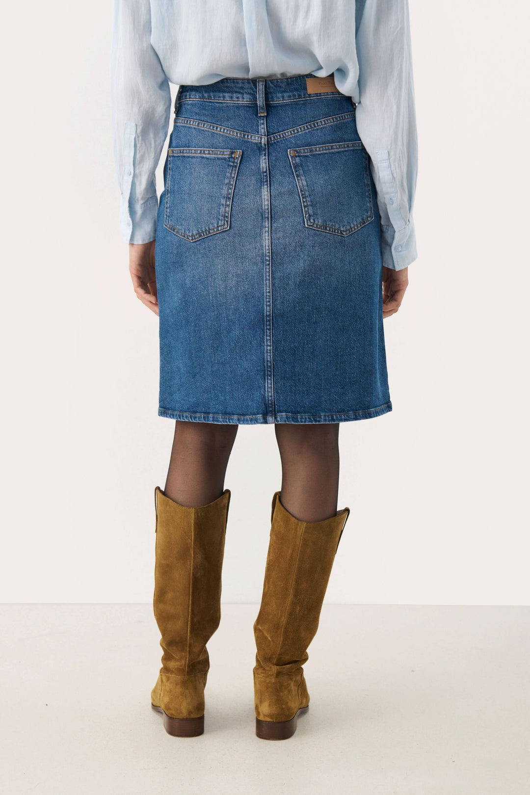 Femme portant une jupe en denim Leja à taille mi-haute, vue arrière, avec des bottes en suède.