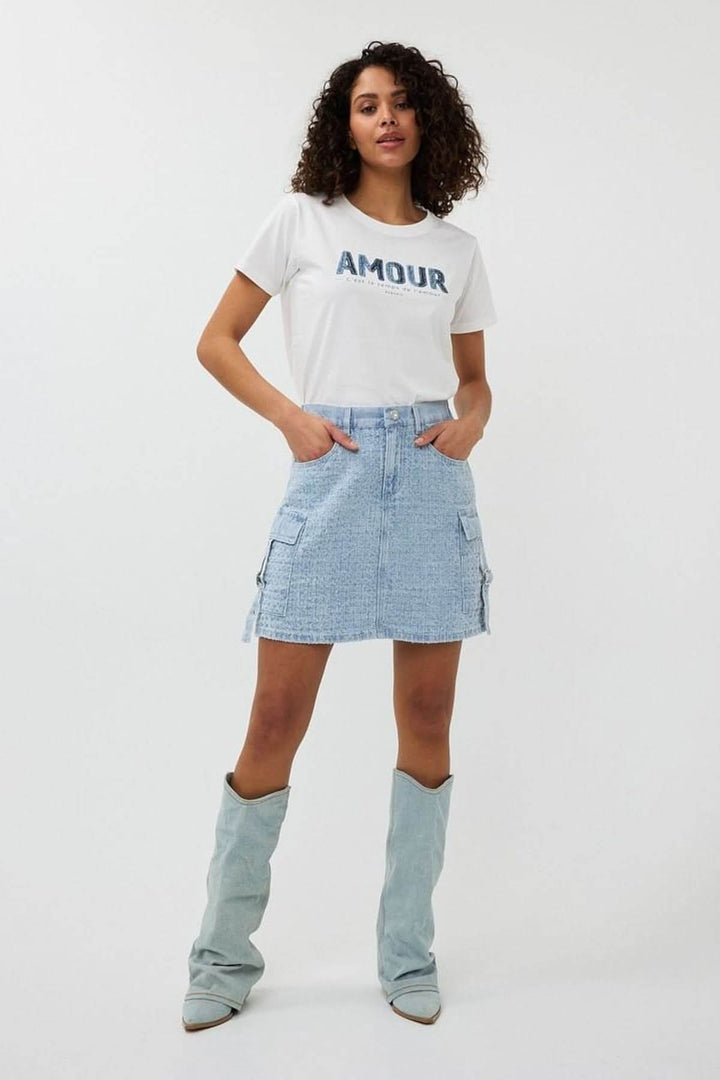 Jupe en denim texturé avec poches cargo, portée avec un t-shirt blanc et des bottes audacieuses.