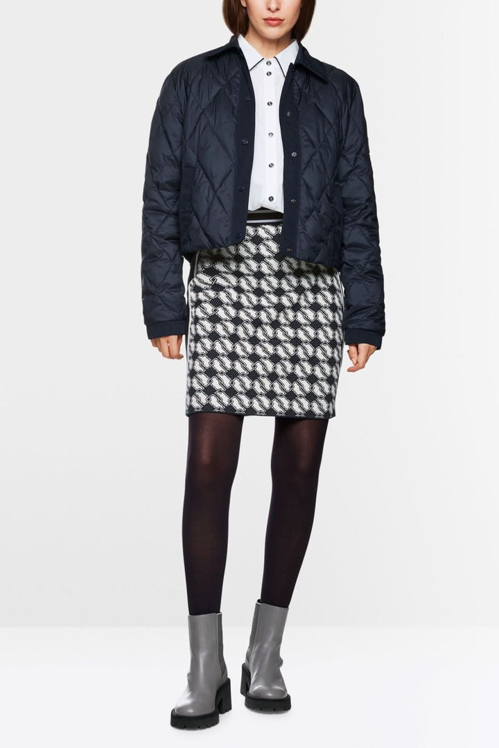 Femme portant une jupe en maille à motif cubique, chemise blanche et veste matelassée, style graphique et moderne.