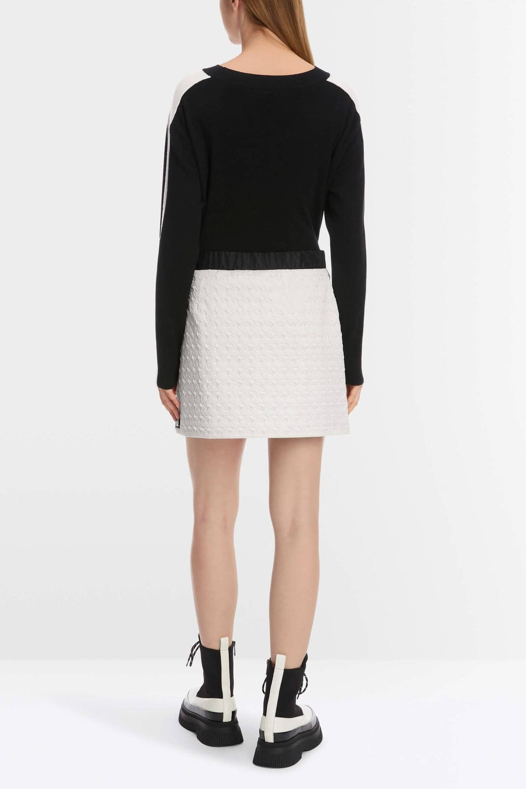 Vue arrière d'une femme portant une mini-jupe matelassée à poches, avec un haut noir et des bottes blanches.