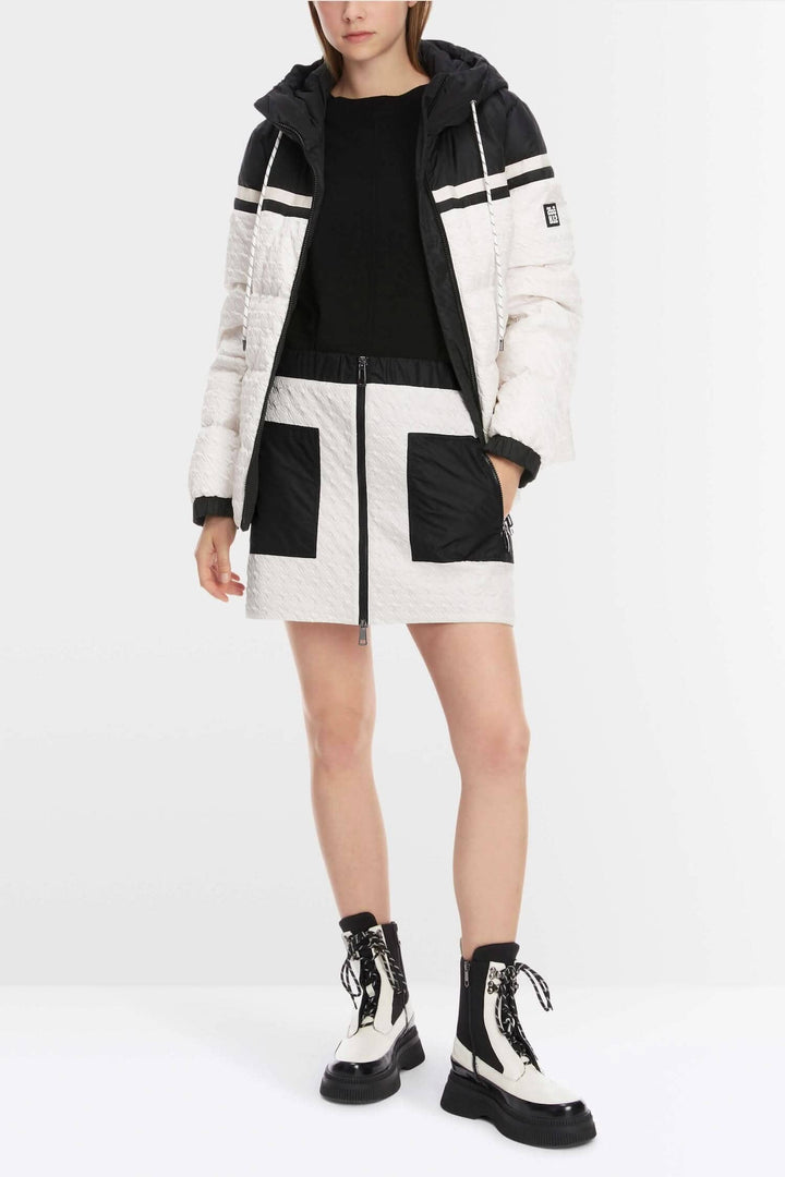 Femme portant une jupe matelassée légèrement évasée avec poches zippées et une veste sportive à capuche.