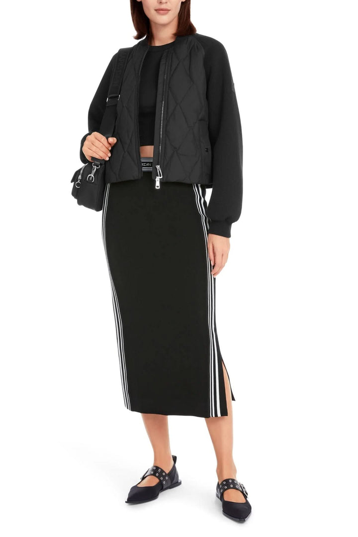 Femme portant une jupe mi-longue noire avec fente latérale et un bomber noir, look décontracté et élégant.