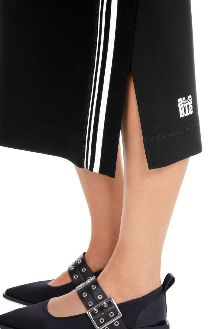 Jupe mi-longue noire avec fente latérale et bandes blanches, portée avec des chaussures élégantes.