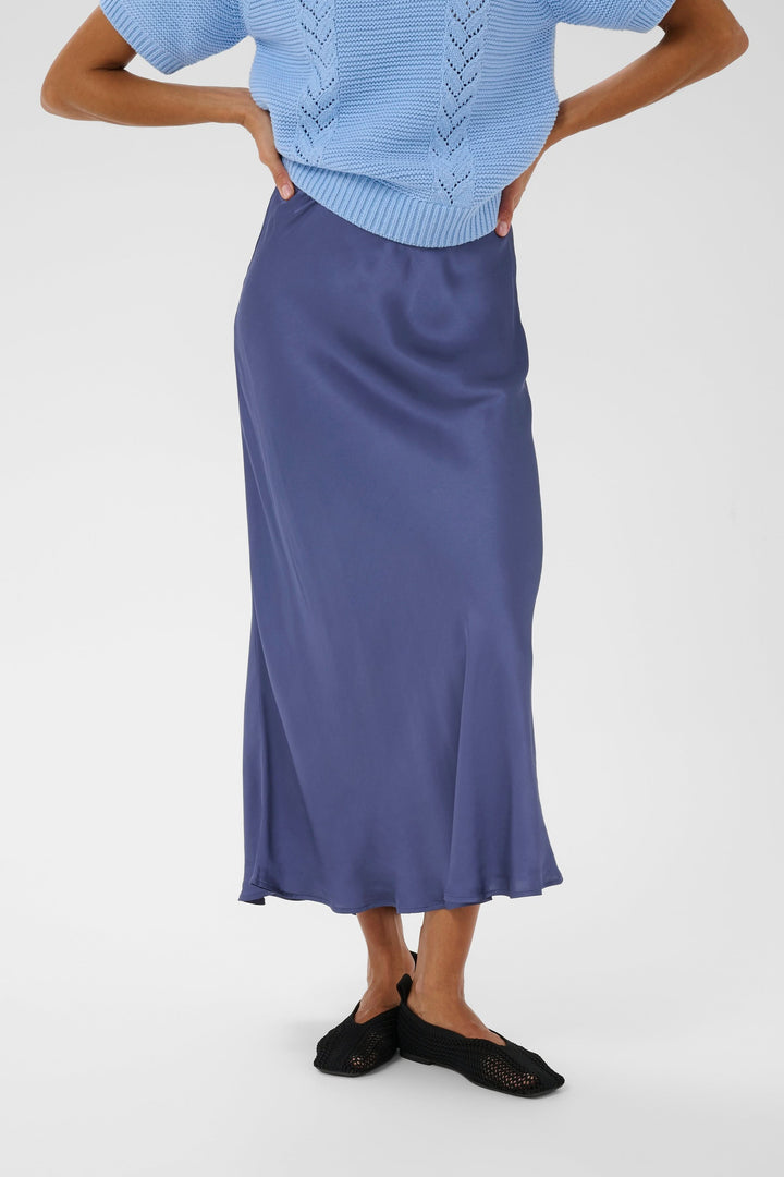 Jupe midi Laurina fluide et élégante avec coupe évasée, portée avec un tricot bleu.