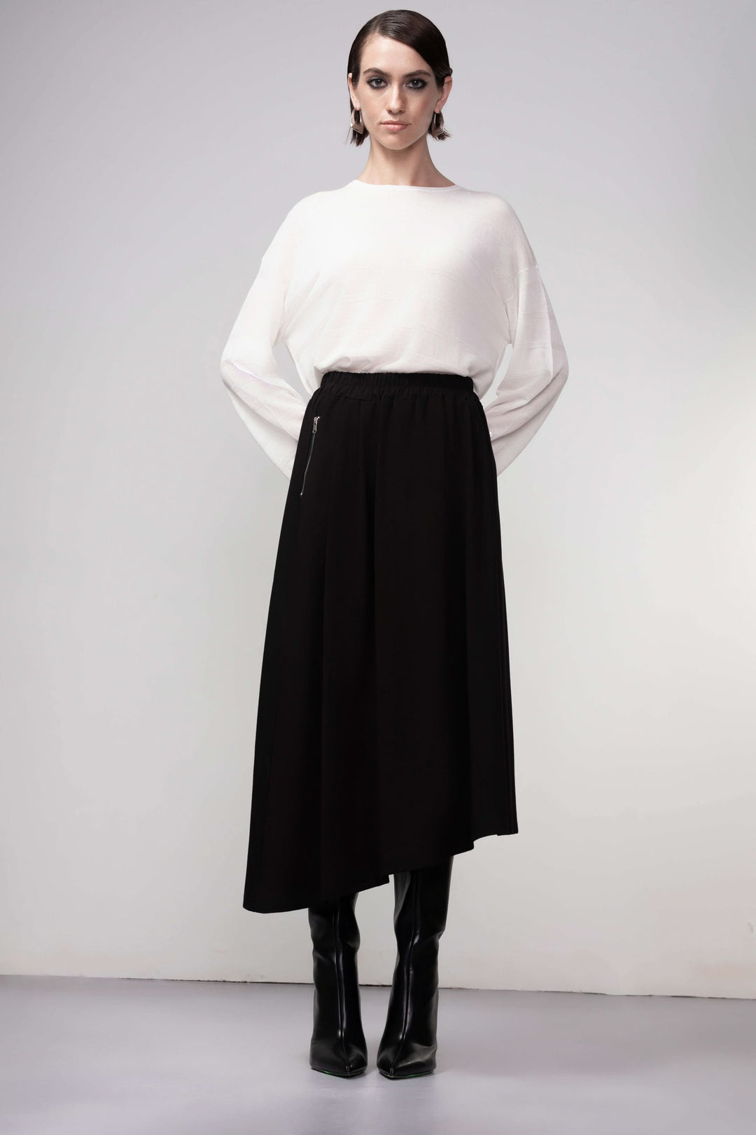 Jupe midi coupe fluide noire avec taille élastiquée et ourlet asymétrique, portée par un mannequin, style élégant et polyvalent.
