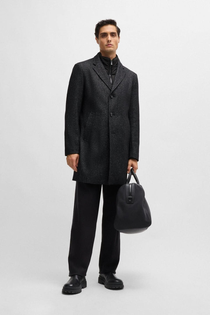 Homme portant un manteau en tweed ajusté BOSS avec fermeture éclair détachable et sac à main noir.