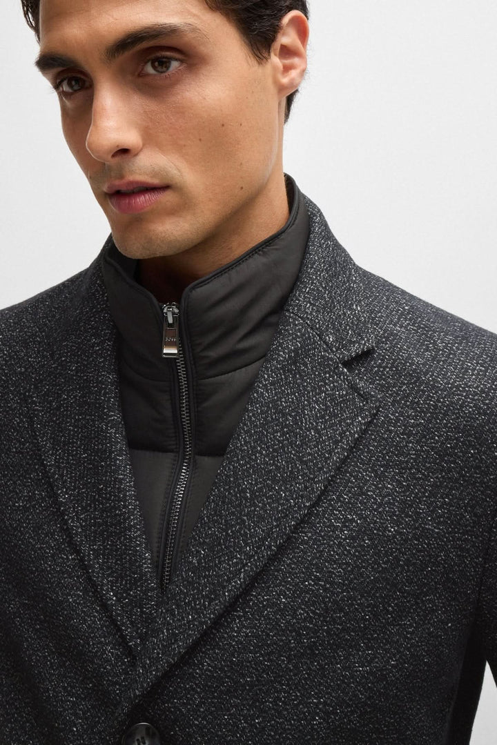 Homme portant un manteau en tweed noir avec fermeture éclair intérieure détachable, style ajusté et élégant.