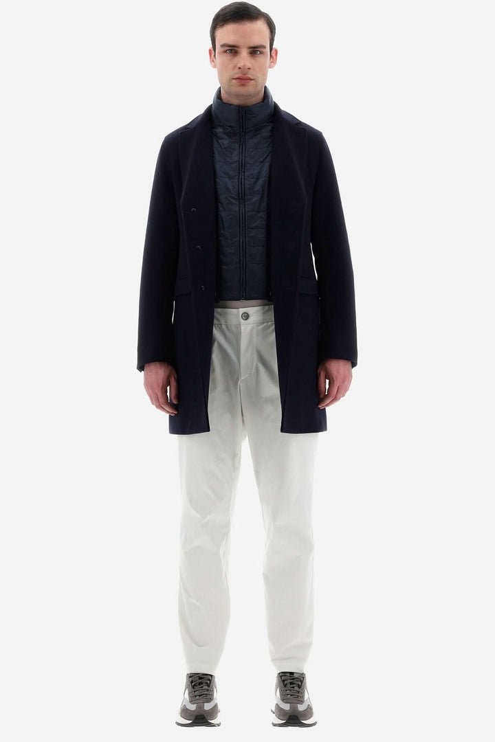 Homme portant un manteau en laine Diagonal bleu avec un col matelassé, pantalon blanc et chaussures grises.