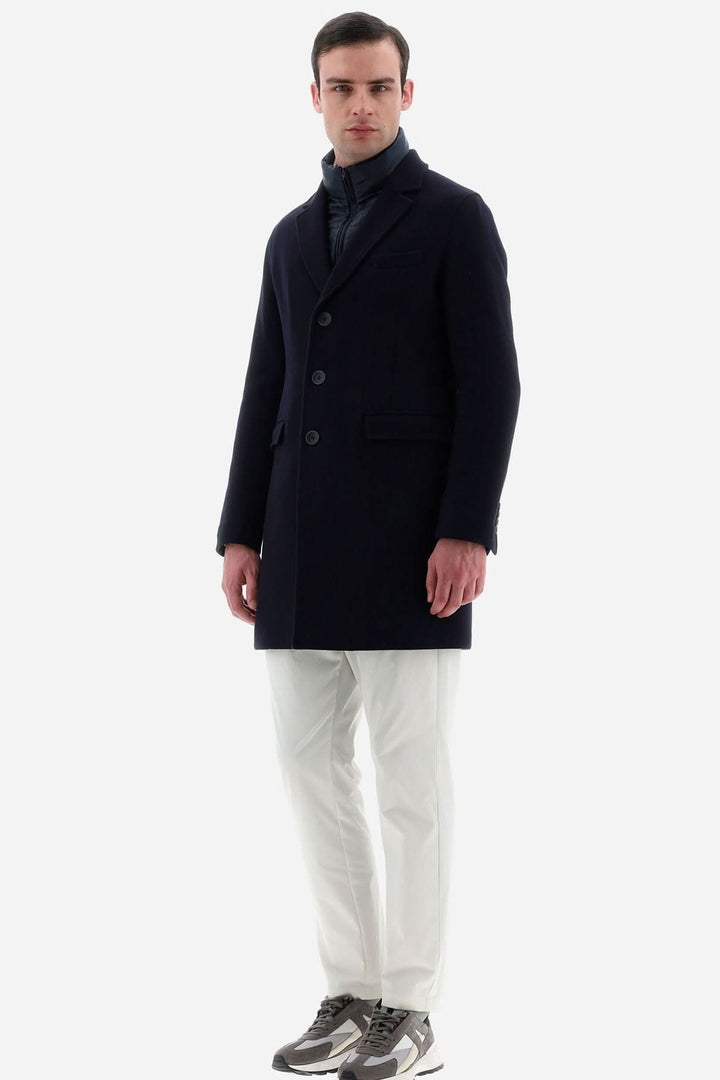 Homme portant un manteau en laine bleu Herno, avec col matelassé et pantalon blanc, style italien élégant.