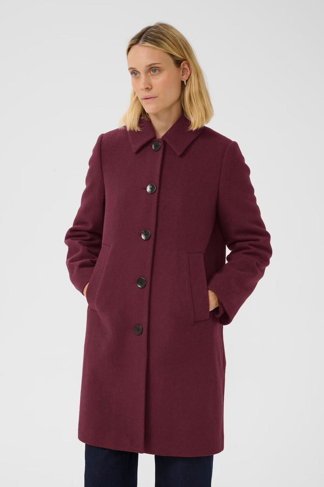 Femme portant un manteau en laine coupe droite bordeaux avec col chemise et boutons apparents, style chic pour l'hiver.