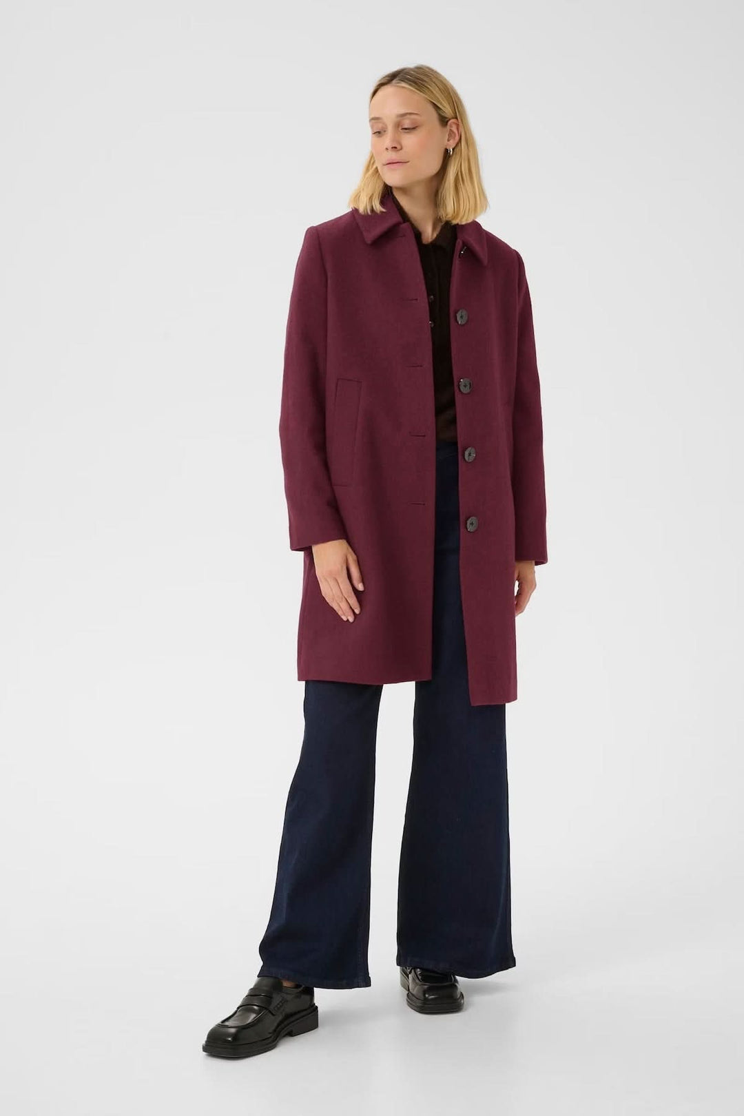 Femme portant un manteau en laine bordeaux à coupe droite avec col chemise et fermeture boutonnée, longueur mi-cuisse, sur un pantalon foncé.
