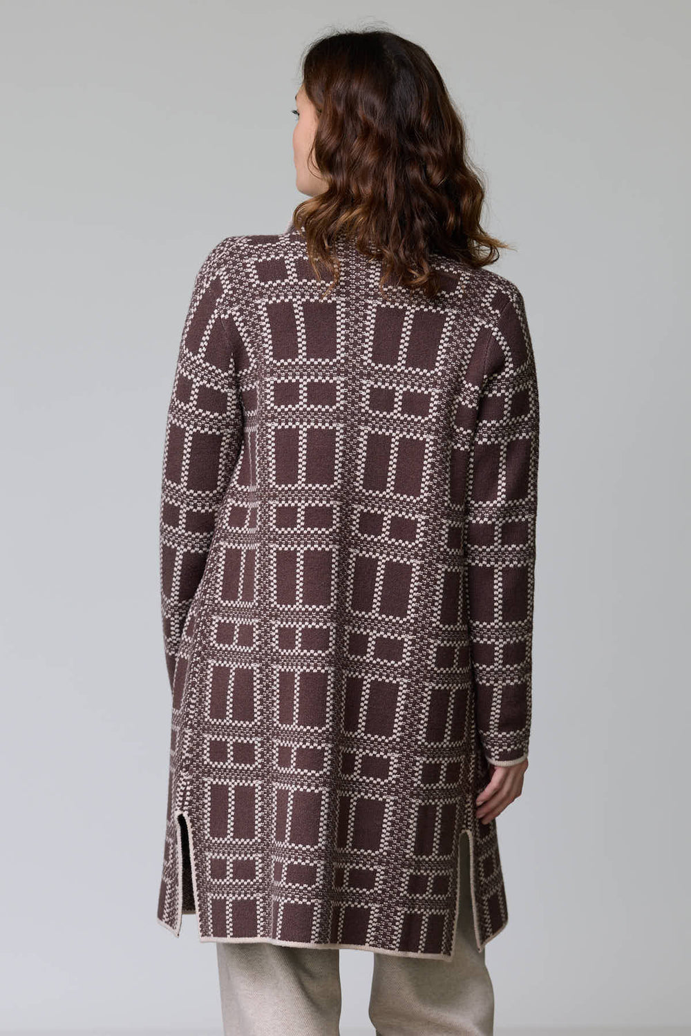 Femme portant un manteau en tricot à motif géométrique bicolore avec coupe droite et longueur mi-cuisse, col ouvert et poches plaquées.