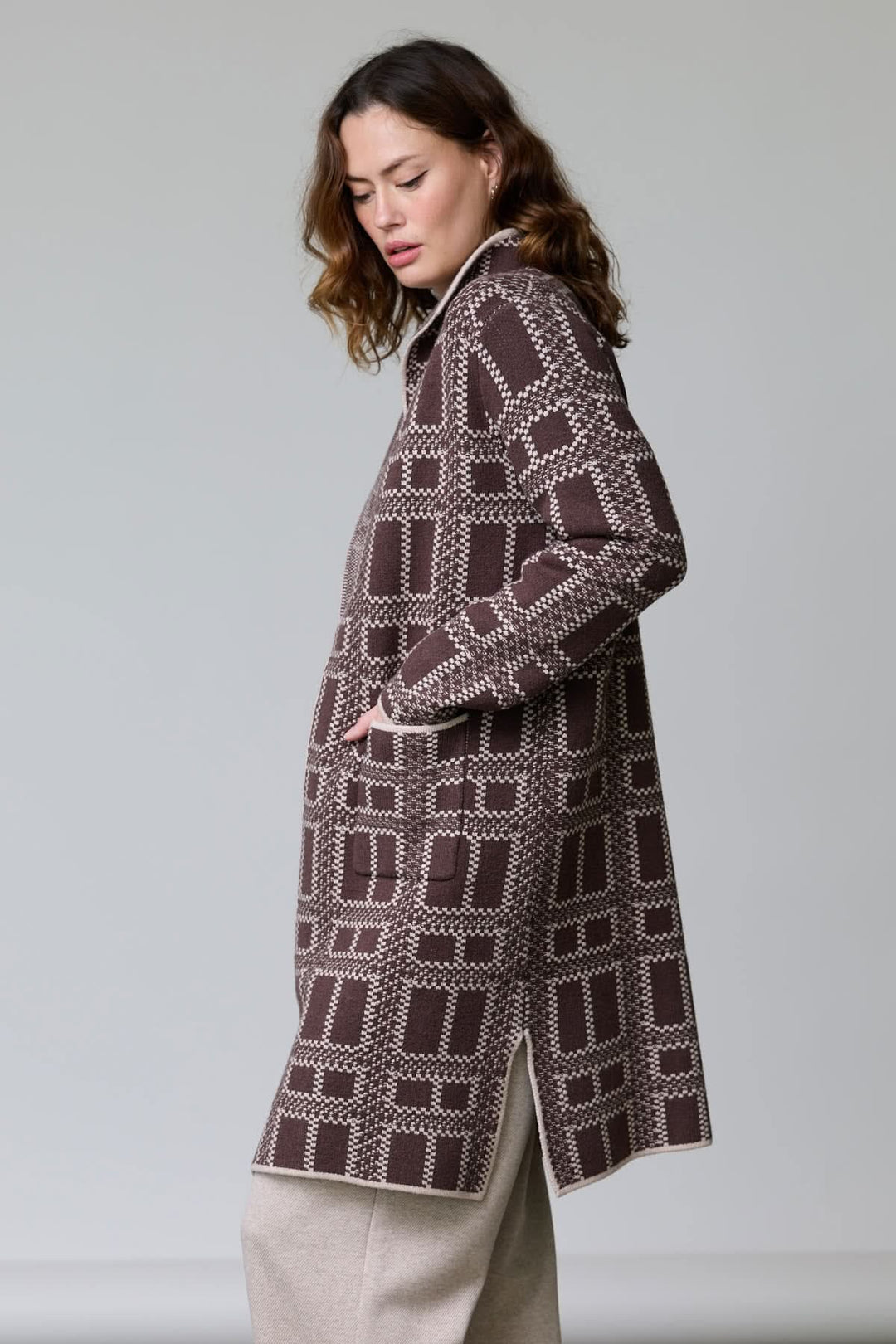 Femme portant un manteau en tricot à motif géométrique avec col ouvert et poches, coupe droite et mi-cuisse, style moderne.