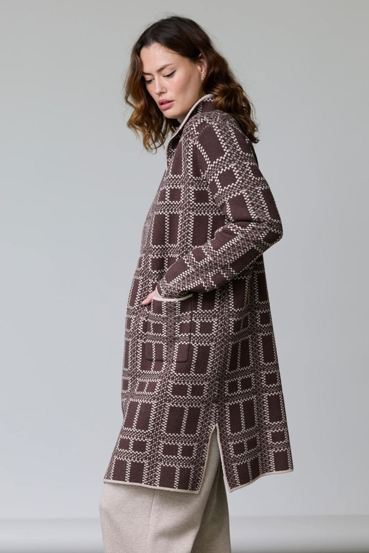 Femme portant un manteau en tricot à motif géométrique avec col ouvert et poches, coupe droite et mi-cuisse, style moderne.