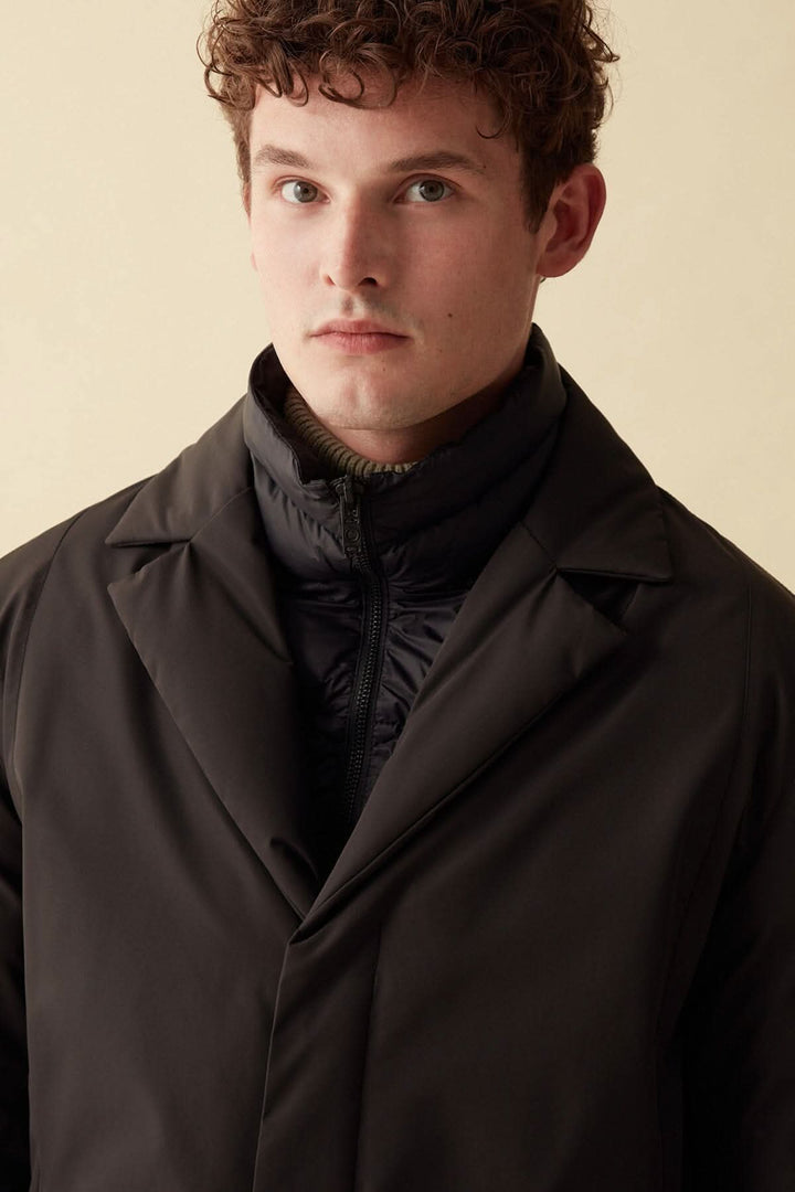 Homme portant un manteau long noir RECYCLED ESSENTIAL, style métropolitain en tissu recyclé.