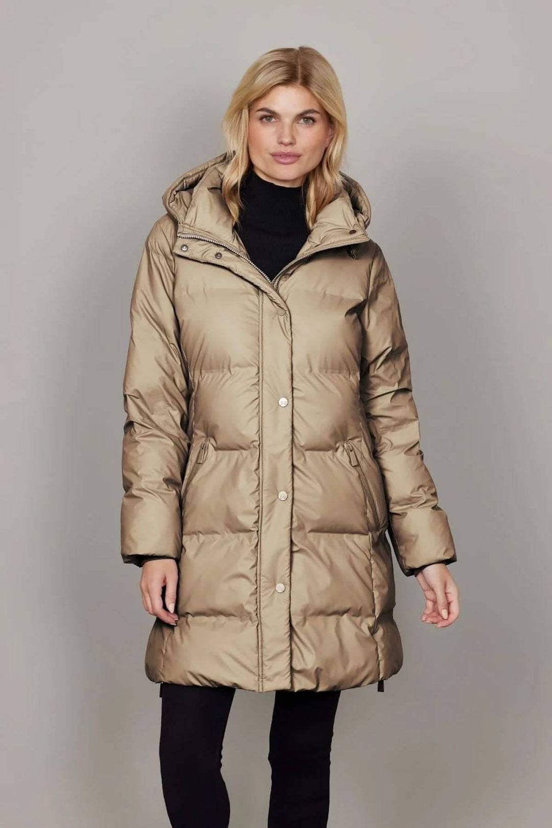 Femme portant un manteau matelassé à capuchon amovible, coupe mi-longue élégante et confortable pour l'hiver, avec tissu déperlant.