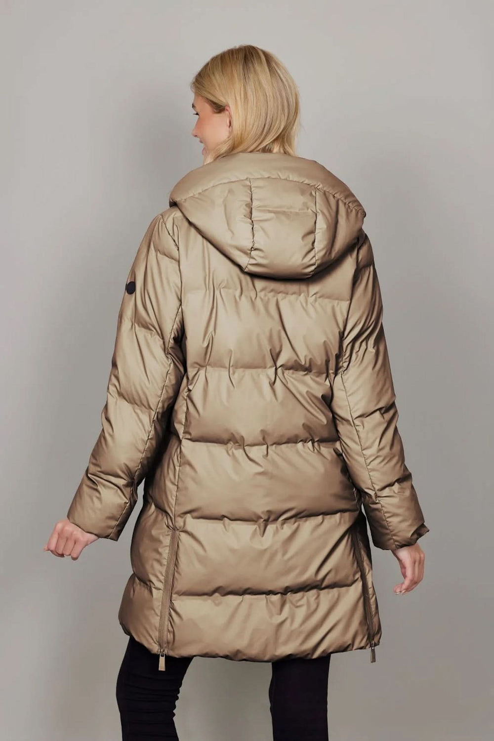 Femme portant un manteau matelassé à capuchon amovible, coupe mi-longue, tissu déperlant, idéal pour l'hiver et les intempéries.
