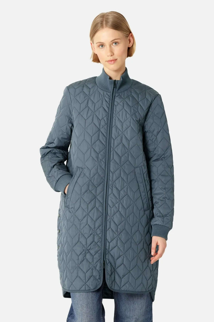 Femme portant un manteau matelassé long à col montant avec motifs géométriques et poches latérales, style urbain et moderne.
