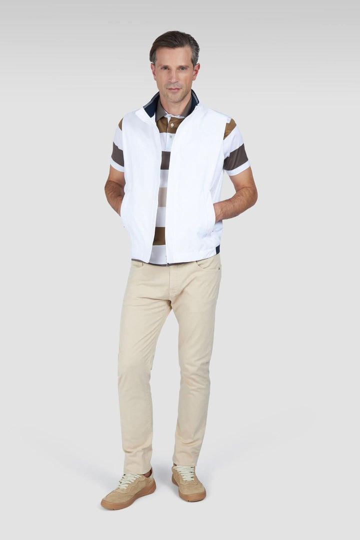 Homme en gilet blanc et polo rayé, portant un pantalon beige, look décontracté et élégant.