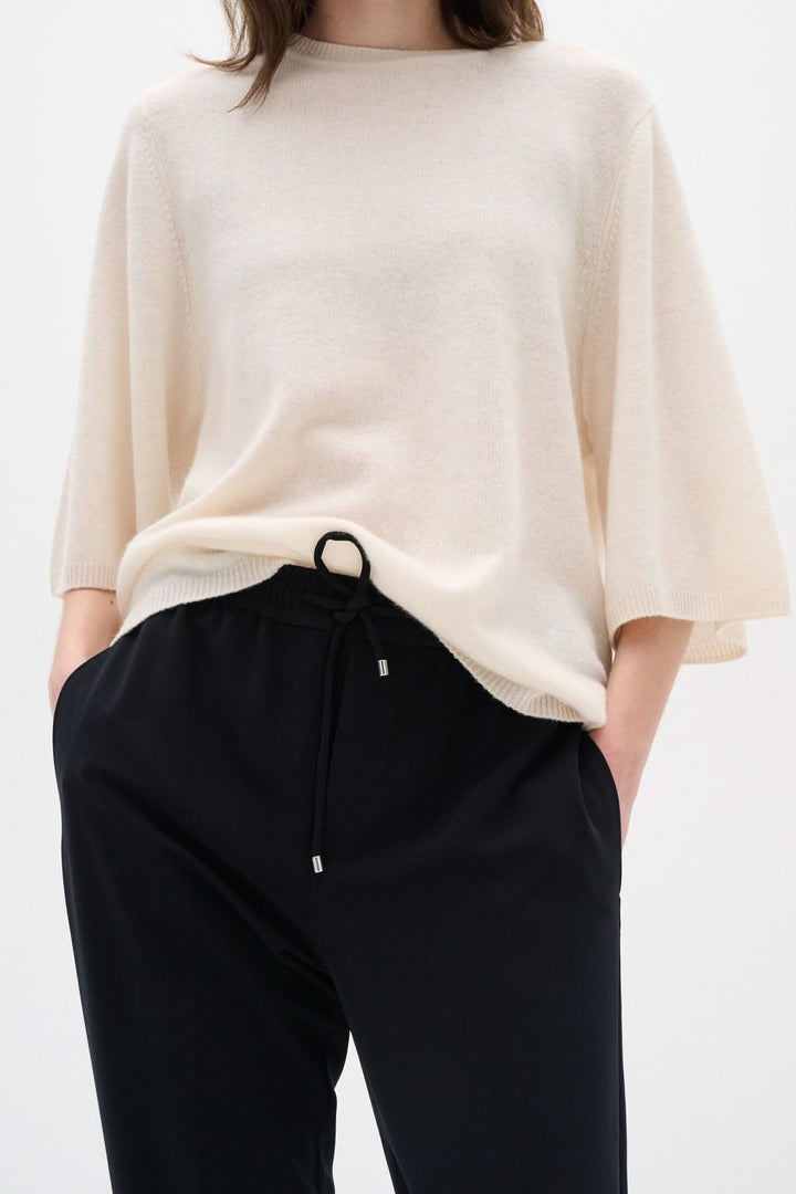 Femme portant un pull crème avec un pantalon noir, style décontracté et élégant, idéal pour un look confortable.