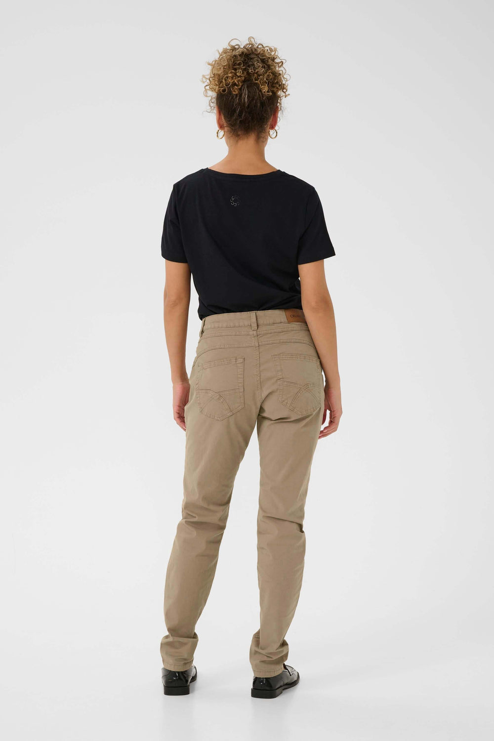 Femme de dos portant un pantalon beige décontracté avec t-shirt noir, style casual chic.
