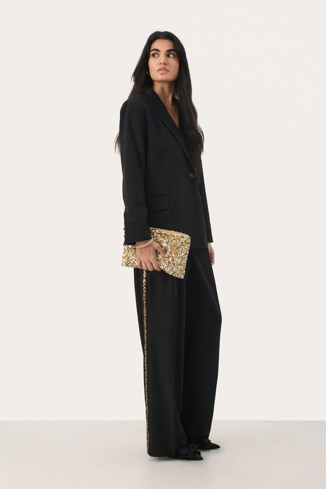 Pantalon CHERRAS noir large avec bande dorée, porté avec blazer et pochette dorée, look élégant et sophistiqué.
