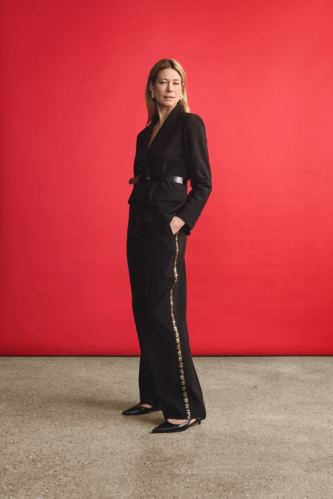 Femme en pantalon noir large avec bande dorée, look élégant sur fond rouge.