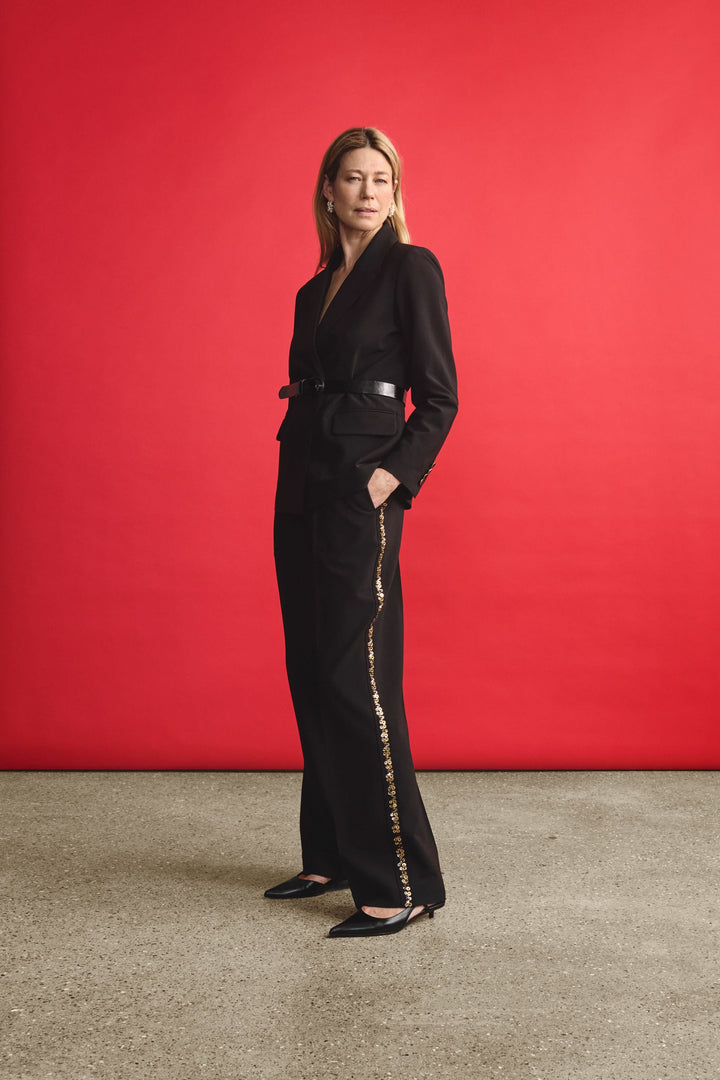 Femme en pantalon noir large avec bande dorée, look élégant sur fond rouge.