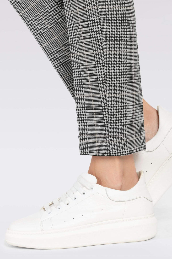 Détail d'un pantalon chino à carreaux avec ourlet, associé à des chaussures blanches élégantes.