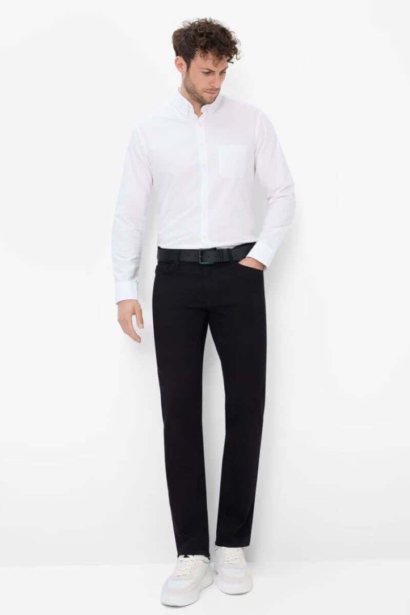 Homme en chemise blanche et pantalon noir, style décontracté avec des baskets blanches, look moderne.
