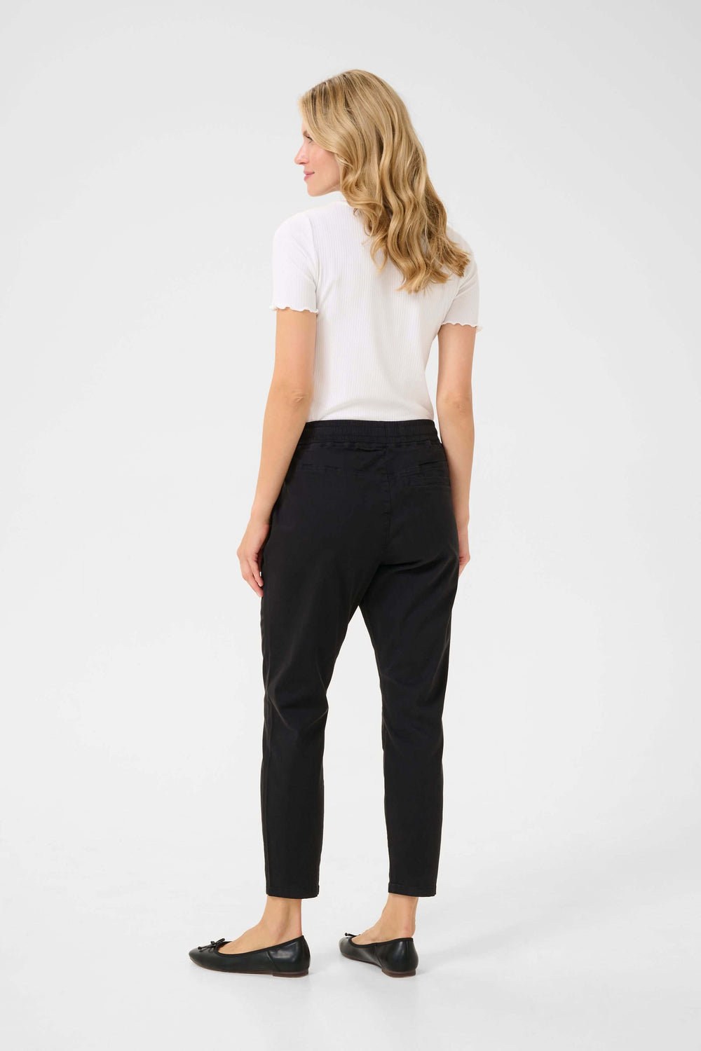 Femme portant un pantalon jogger chic noir avec taille élastique, vu de dos, associé à un t-shirt blanc.