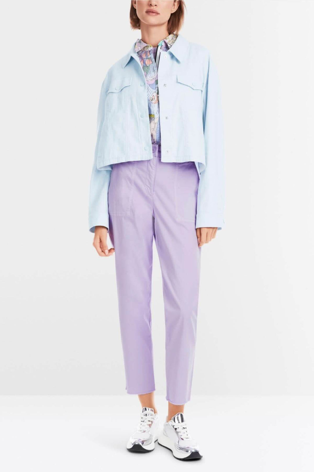 Femme portant une veste en jean bleu et un pantalon lilas, style décontracté et moderne, avec des chaussures blanches.