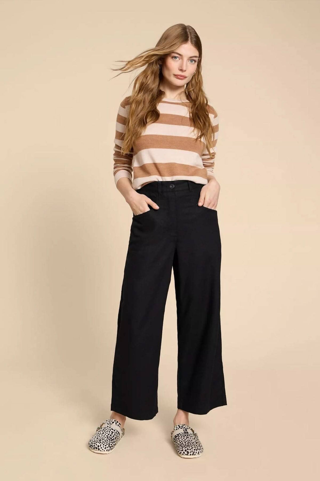 Femme portant le pantalon Harper à jambe large, avec un pull rayé, pose devant un fond neutre.