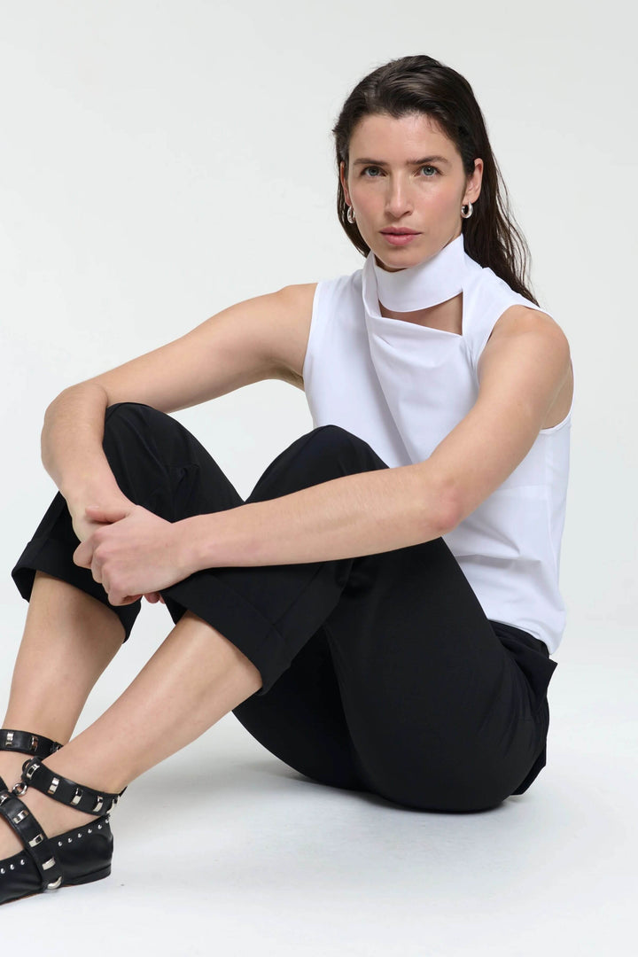 Femme assise en pantalon noir et top blanc élégant, affichant un style chic et décontracté.