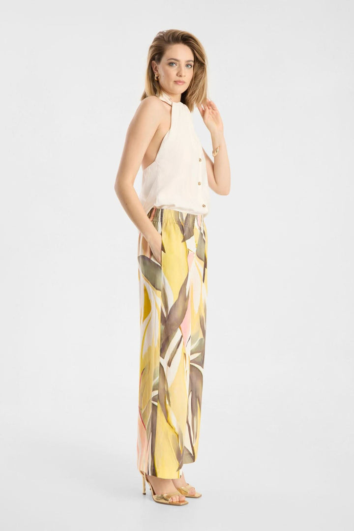 Femme portant un Pantalon Lizett fluide imprimé à taille élastique avec un haut blanc, posant de profil, sur fond blanc élégant.