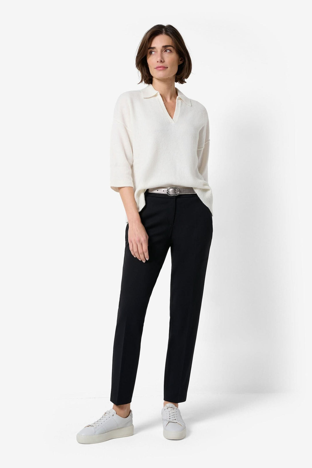 Femme portant un pantalon noir avec une blouse blanche, chaussures décontractées, style chic et confortable.