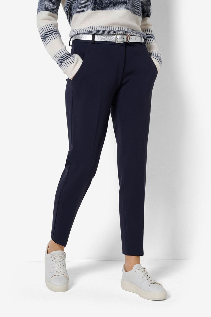 Pantalon chino femme bleu marine avec ceinture, porté avec un pull à rayures et des sneakers blanches.