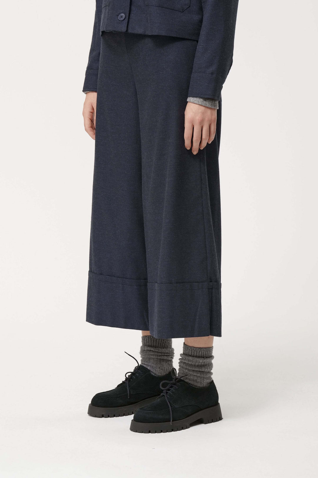 Pantalon Sophio ample façon culotte, taille élastique, style contemporain, porté avec chaussures noires et chaussettes grises.